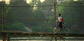 Kid riding a bike over a wooden bridge in Thailand.