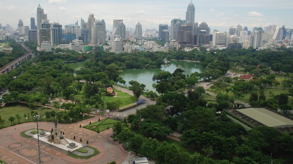 A lush city landscape with trees and a lake in front of skyscrapers
