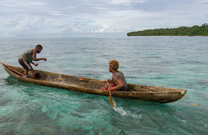 Two fishermen putting nets out in a small canoe-like boat