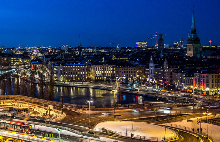 A dynamic aerial view of Stockholm at night, with cars on winding roads and old buildings lit up in the background.