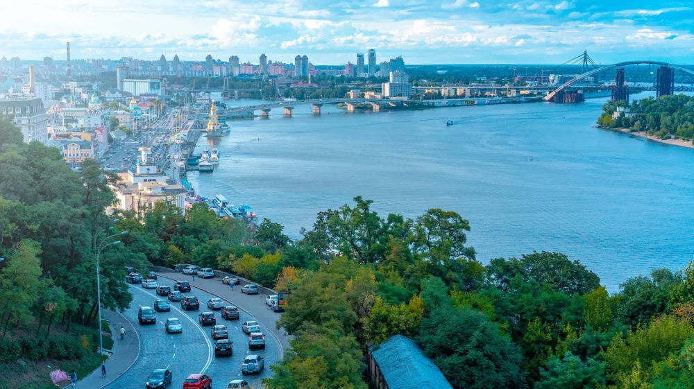 Big landscape view of a wide blue river, two major bridges crossing at a fork, with major road and a city dominating the left-hand side of the show.