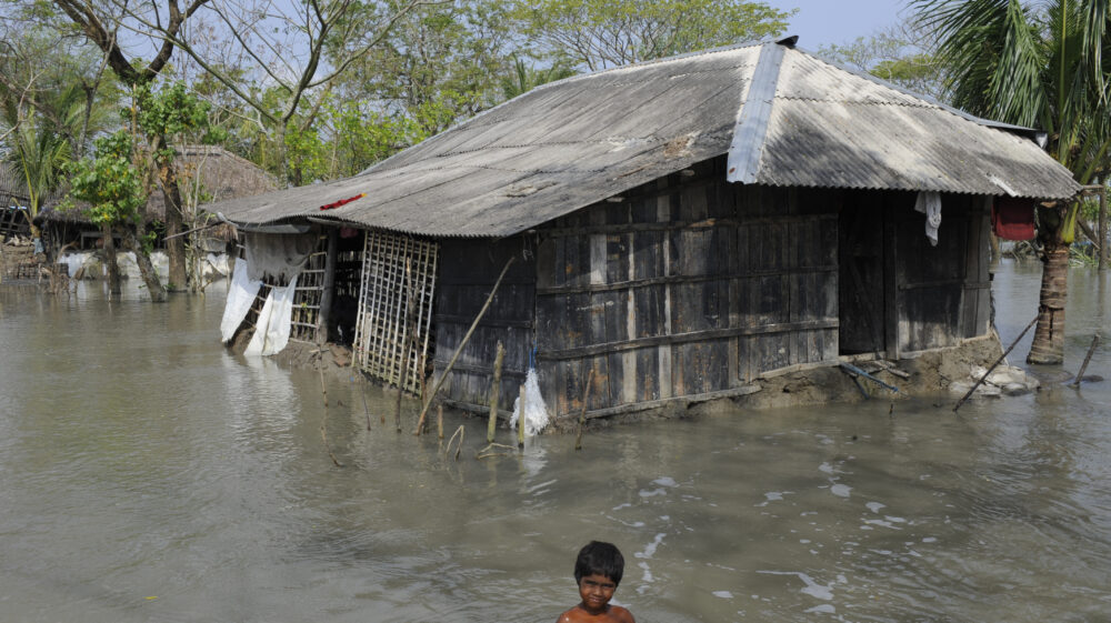 A child sits in floodwater in front of a house in Bangladesh.