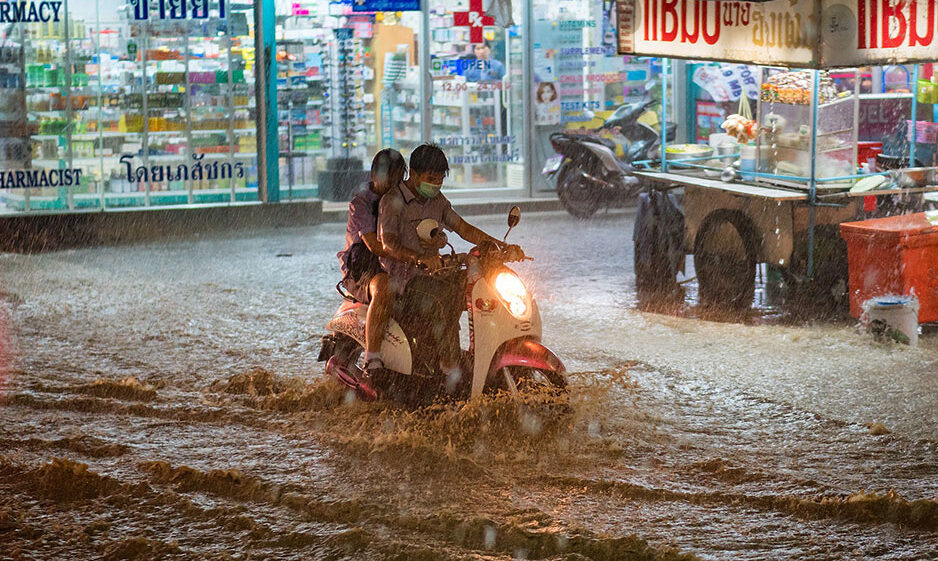 Two people on a scooter on a heavily flooded road