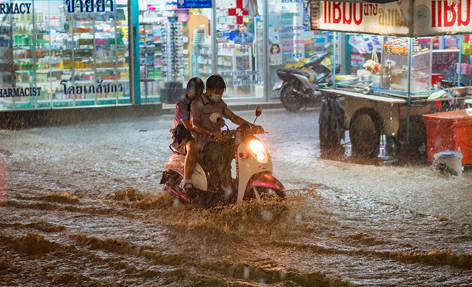 Two people on a scooter on a heavily flooded road