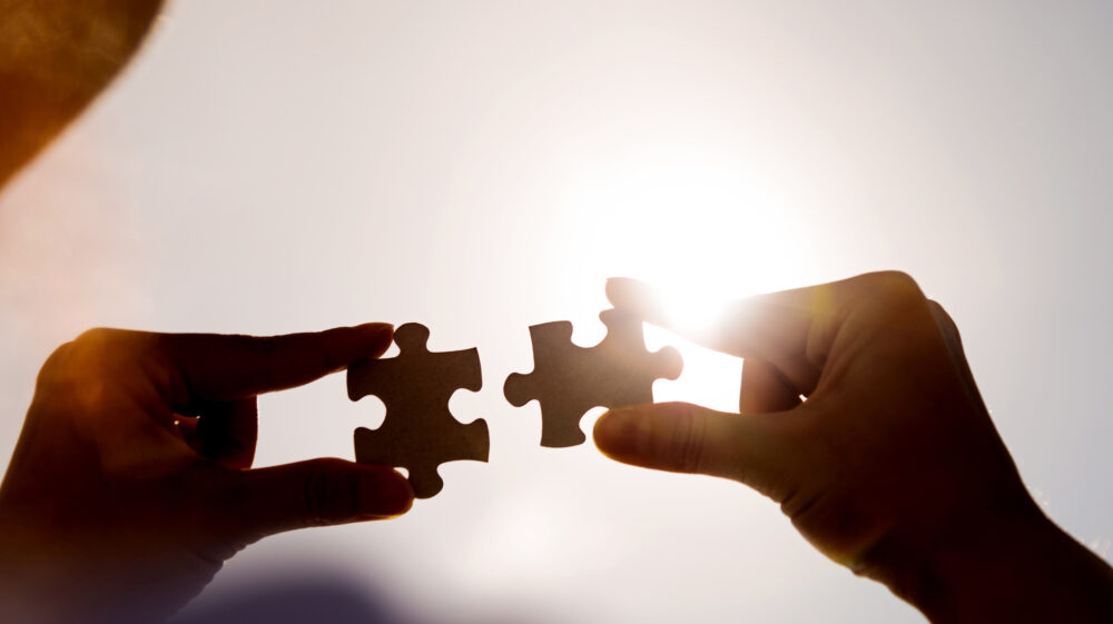Woman hands connecting two jigsaw puzzle pieces against sunset sky.
