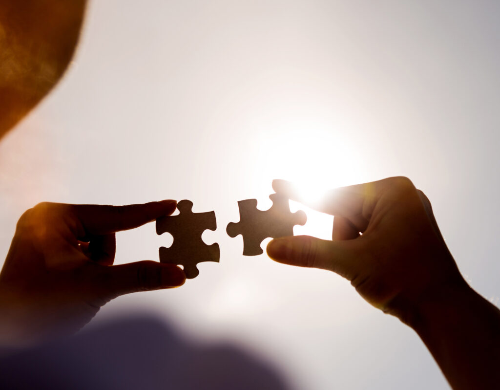 Woman hands connecting two jigsaw puzzle pieces against sunset sky.
