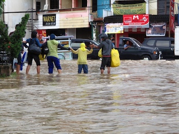 Five people holding hands and wading through a flood in an urban area