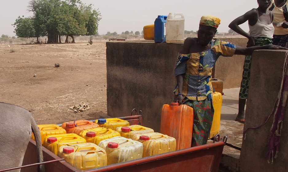 Woman lifting jerry cans into trailer in Centre-East, Burkina Faso