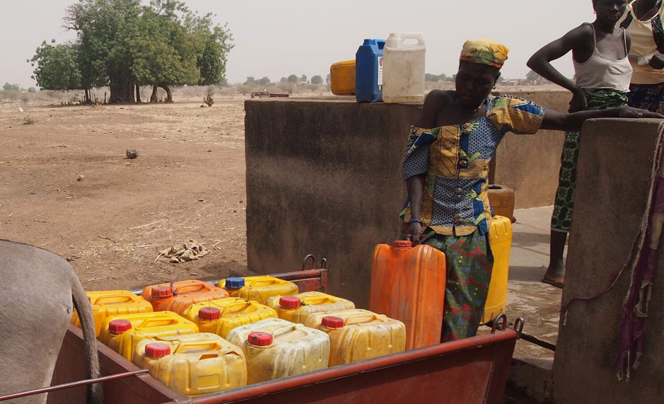 Woman lifting jerry cans into a trailer in Burkina Faso