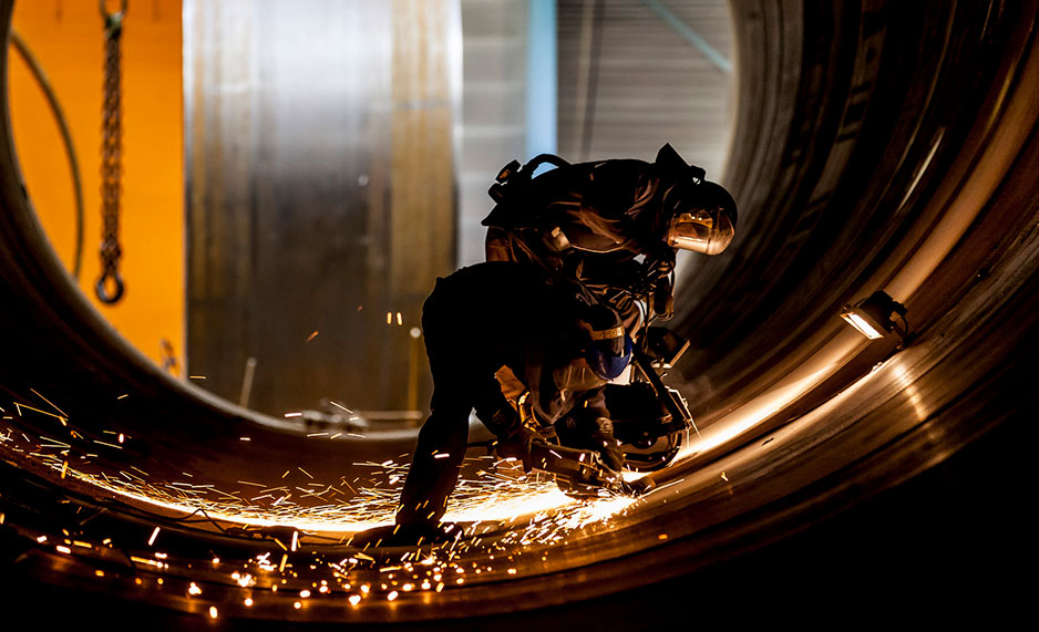 Two people welding steel while standing in a large metal tube.