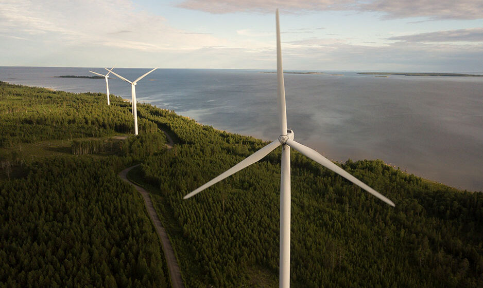 Wind turbines built amongst trees near a body of water.