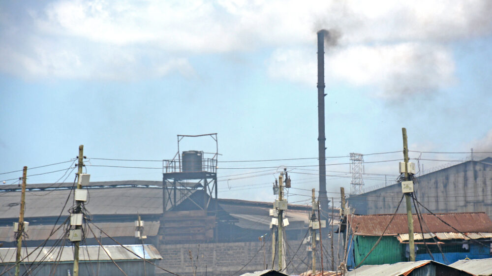 A factory chimney spews smoke over the rooftops of nearby homes in Mukuru
