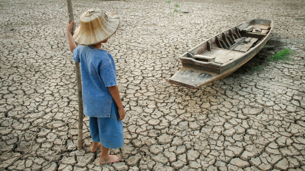 Child standing near a wooden boat on cracked earth. Metaphor for climate change.