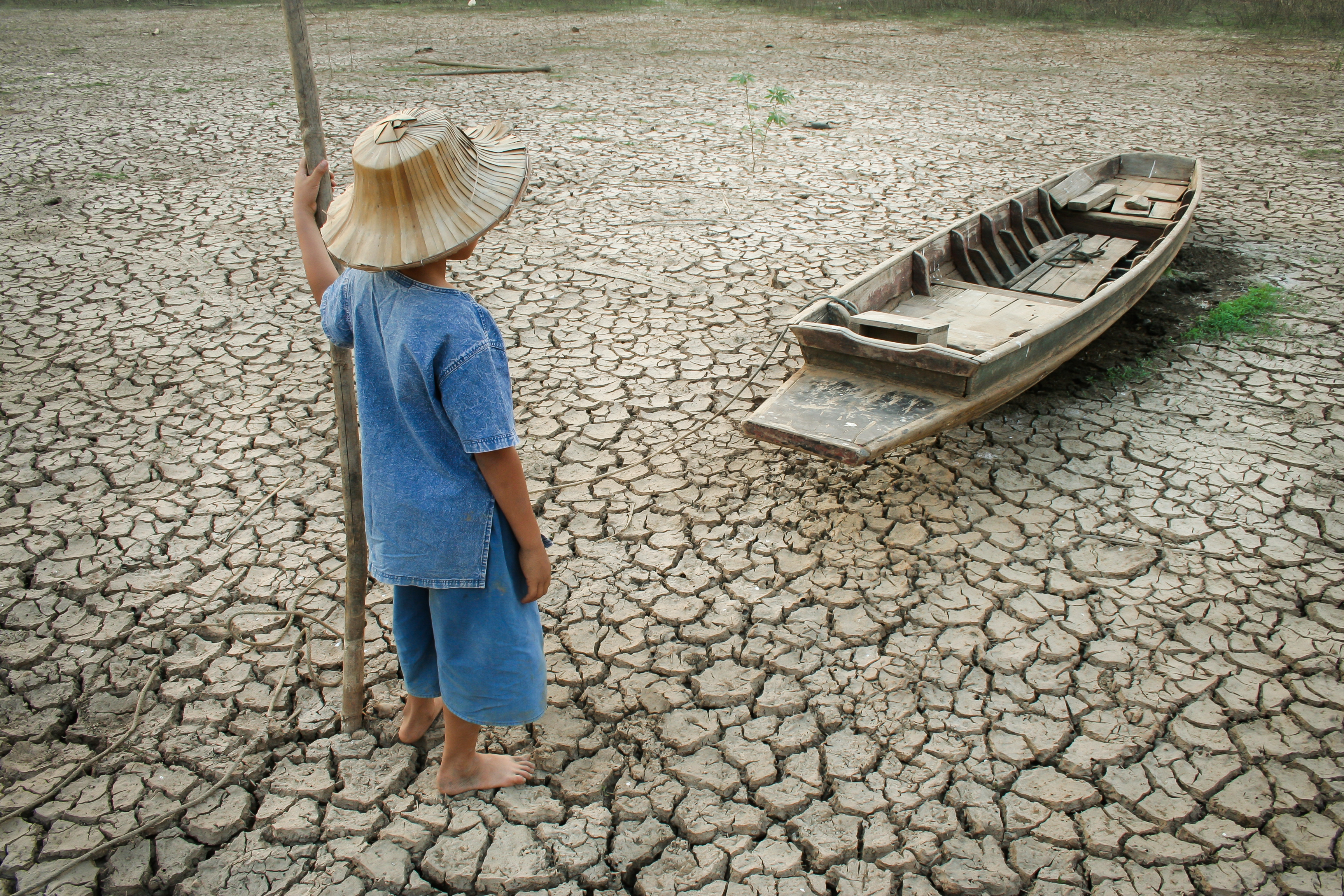 Child standing near a wooden boat on cracked earth. Metaphor for climate change.