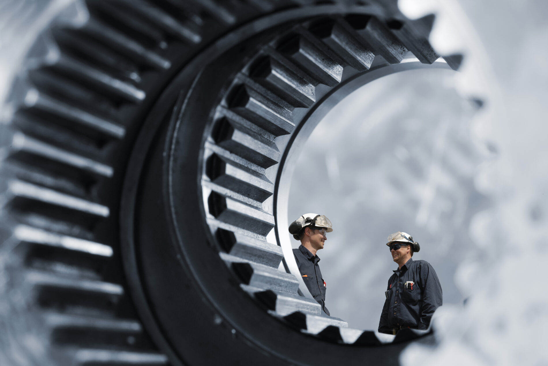Two industry workers standing inside a giant gear, steel works industry