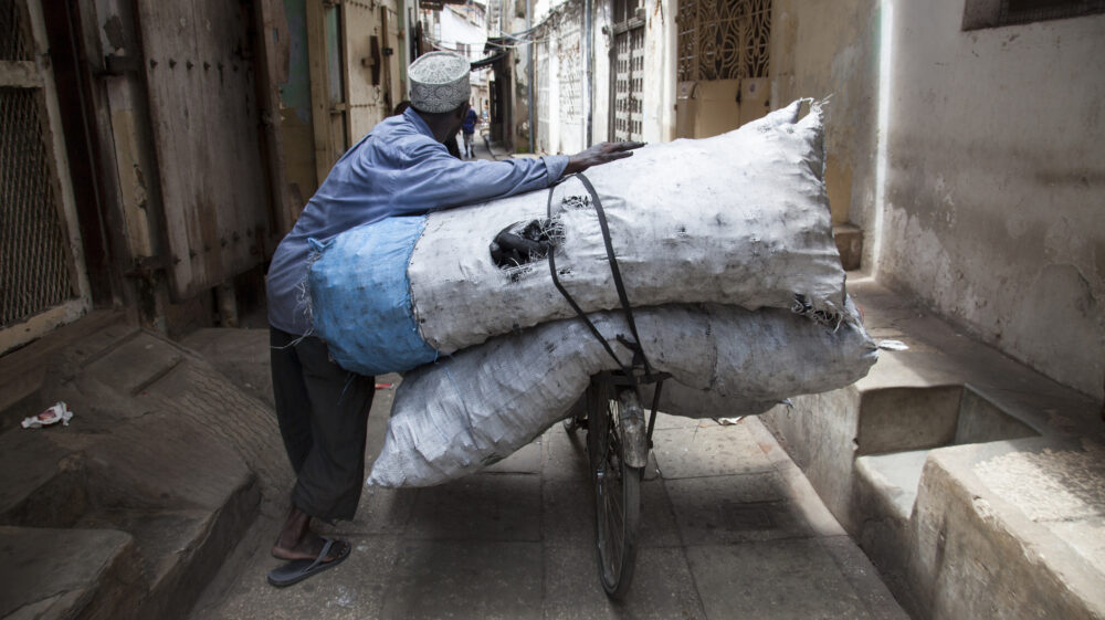 Old man carrying huge sacks of coal on his bicycle in a narrow street of Stone Town, Zanzibar, Tanzania, East Africa.