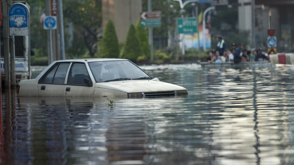 Flooded car with rescue boat full of people in the background