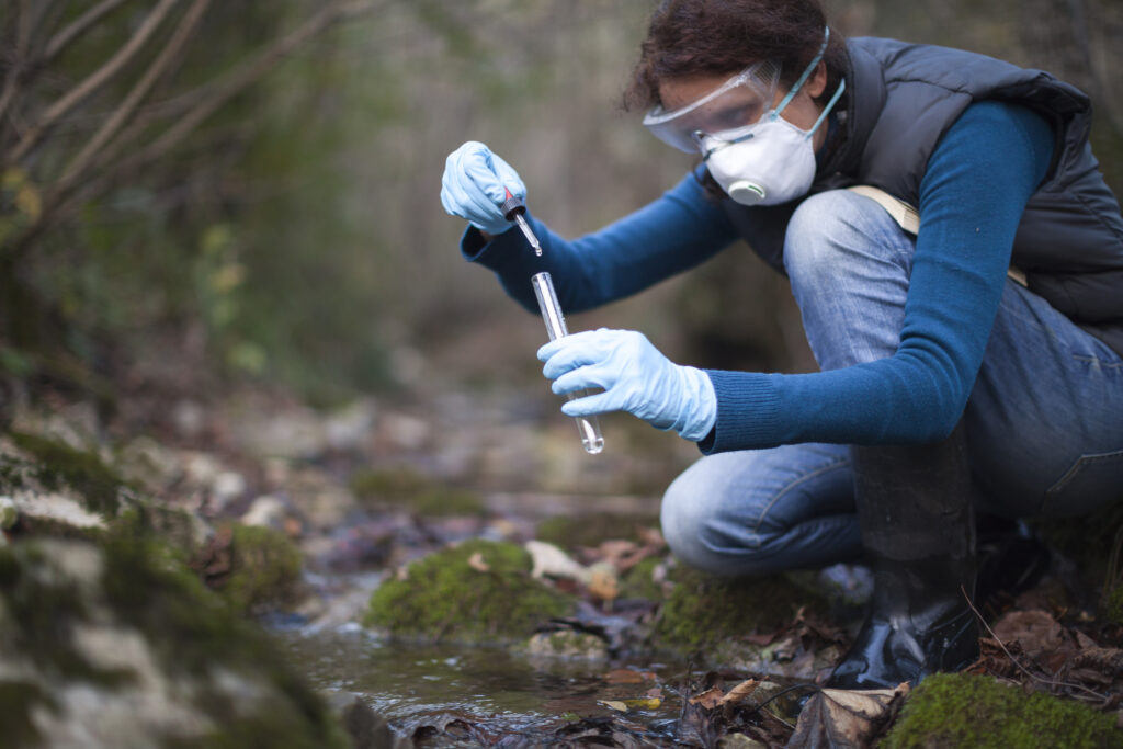 Biology researcher taking a water sample from a stream.
