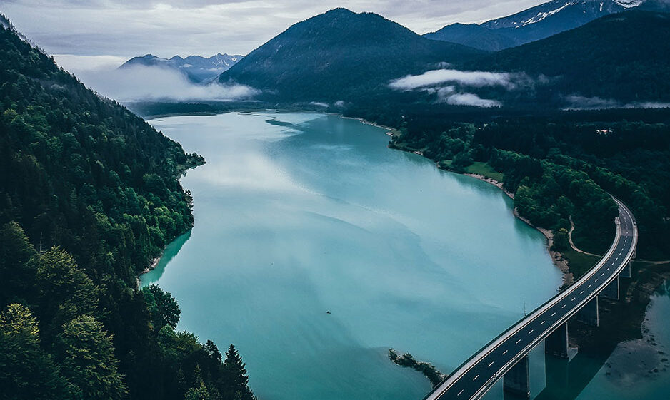 Aerial view of a bridge over river amidst mountains and a cloudy sky