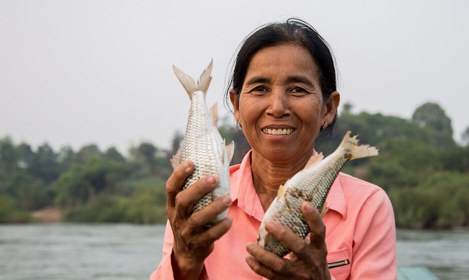 A smiling woman holds two freshly-caught fish