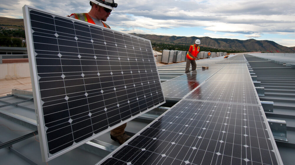 Construction workers install solar panels on a roof