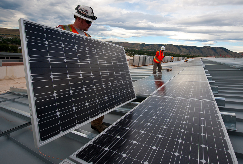 Construction workers install solar panels on a roof