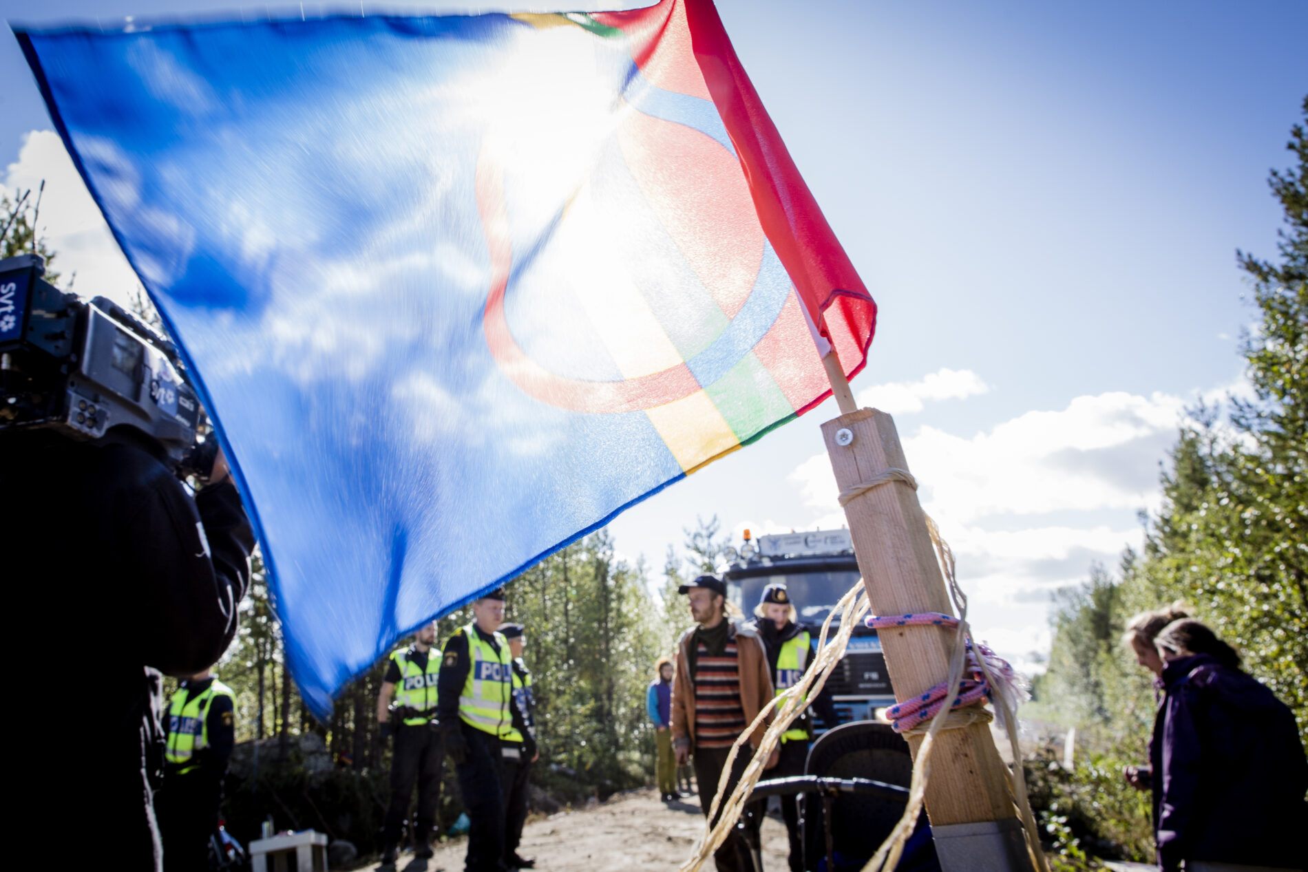 The Sámi flag waves in the foreground, with police in the background.
