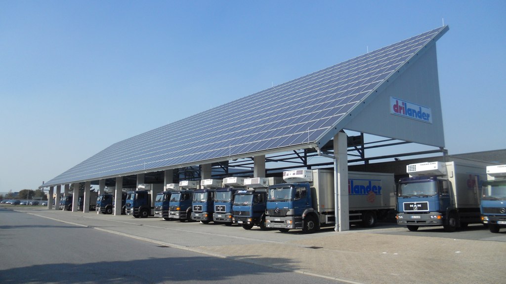 a line of trucks parked and recharging under a roof covered with solar panels
