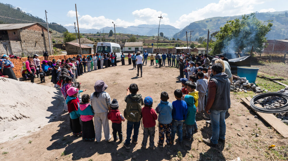 People standing in a circle outdoors, near buildings, focused on a person in the centre.