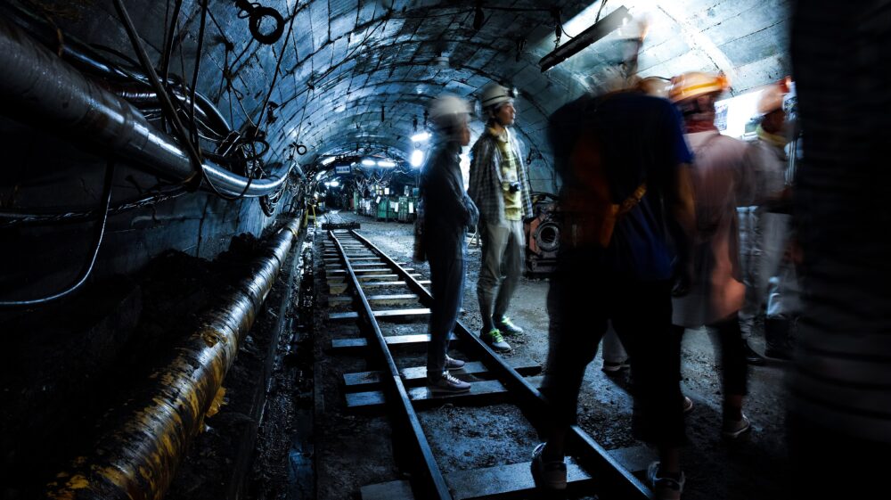 Several individuals in hard hats stand inside a mining tunnel
