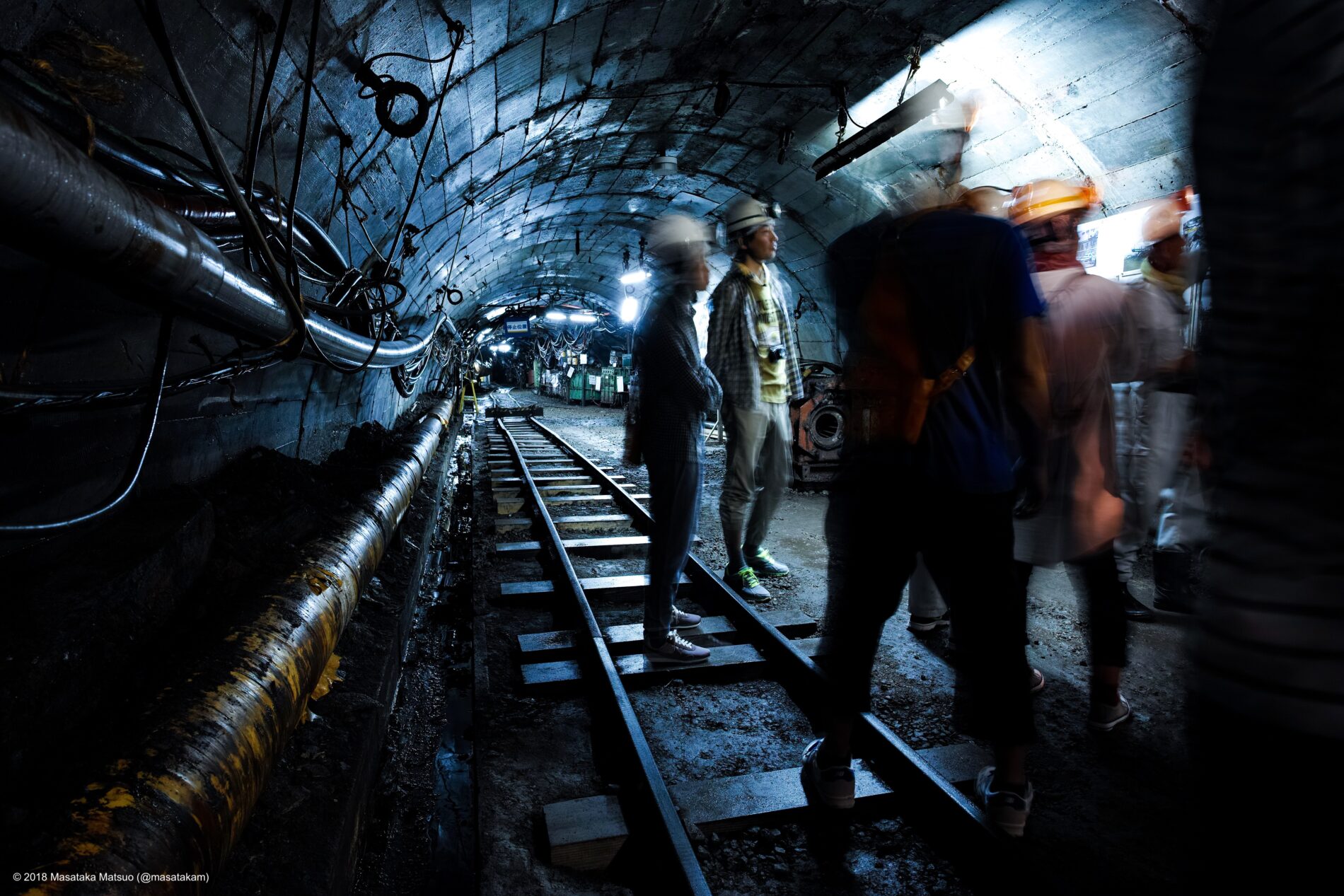 Several individuals in hard hats stand inside a mining tunnel