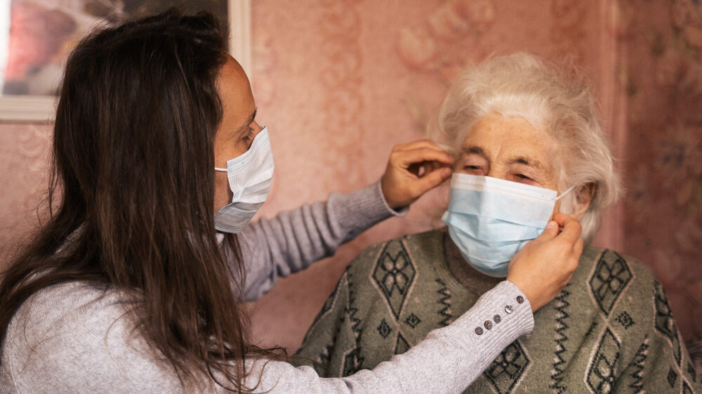 Young woman with her grandmother, discussing the coronavirus, both with protective masks on their faces.