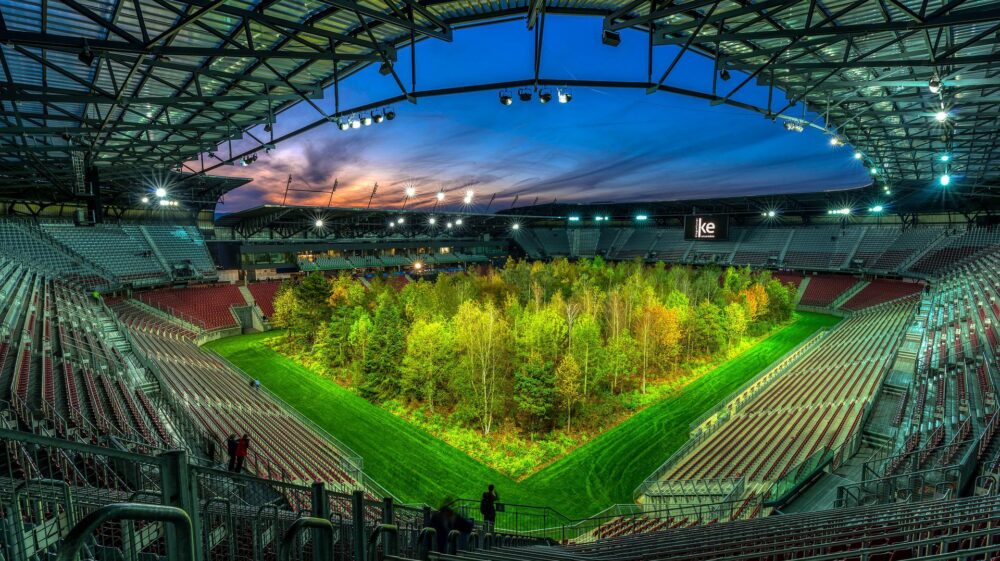 Composite of green forest in stadium at dusk under light purple and blue sky and stadium lights, Klagenfurt, Austria