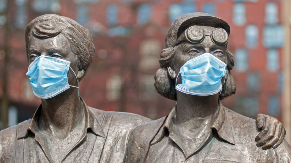 A steel sculpture of two women wearing face masks.