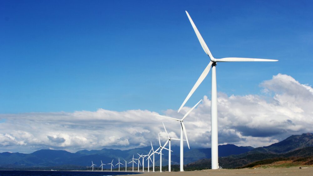 White wind turbines on grey sand near body of water during daytime