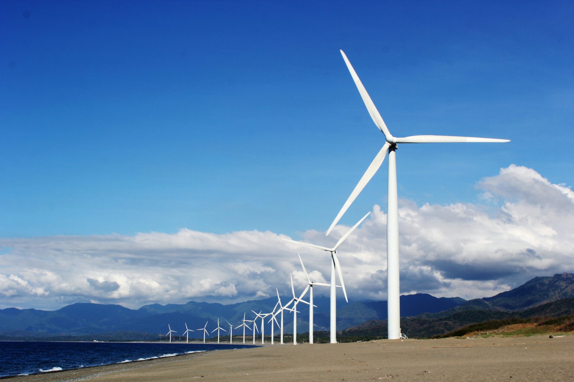 White wind turbines on grey sand near body of water during daytime