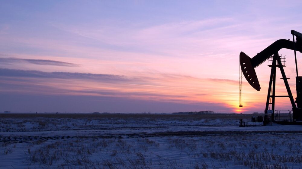 Oil drilling rig and pumpjack on flat plain in Canadian oil fields at sunset under purple sky