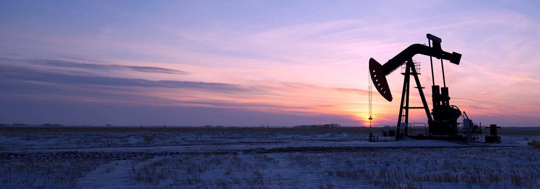 Oil drilling rig and pumpjack on flat plain in Canadian oil fields at sunset under purple sky