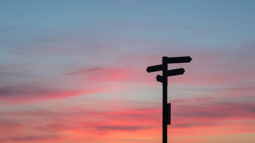 A signpost points in different directions in front of a sunset