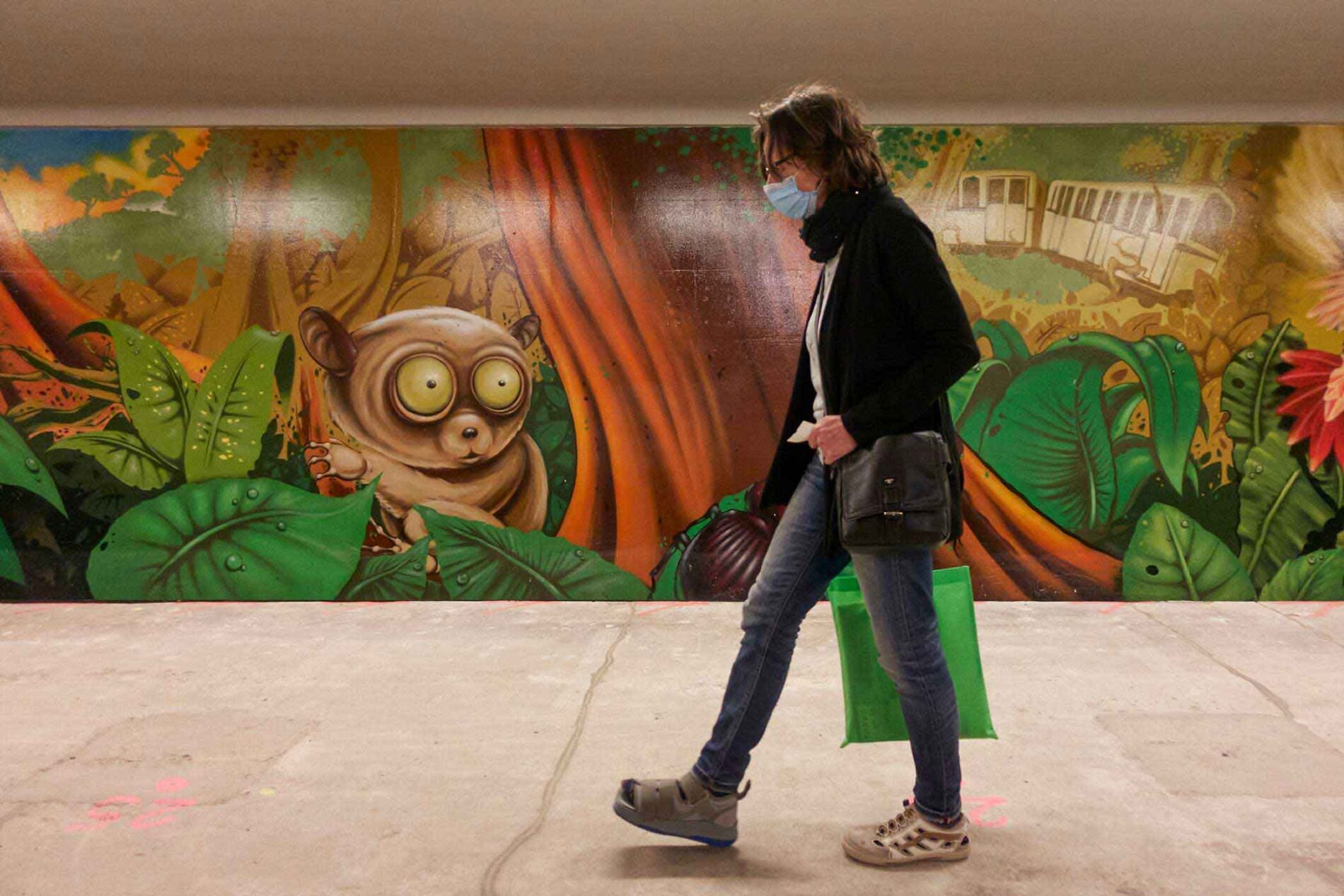 A person wearing a mask walks in front of a painted mural showing a jungle scene.