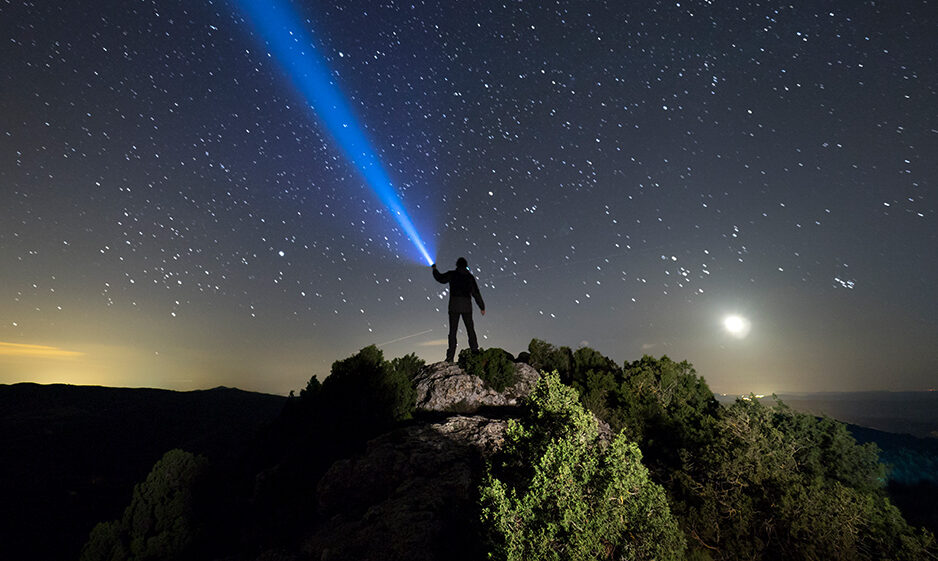 Silhouette of a man on the top of a mountain in the night, with a lantern in the hand doing a beam of light on a sky of stars