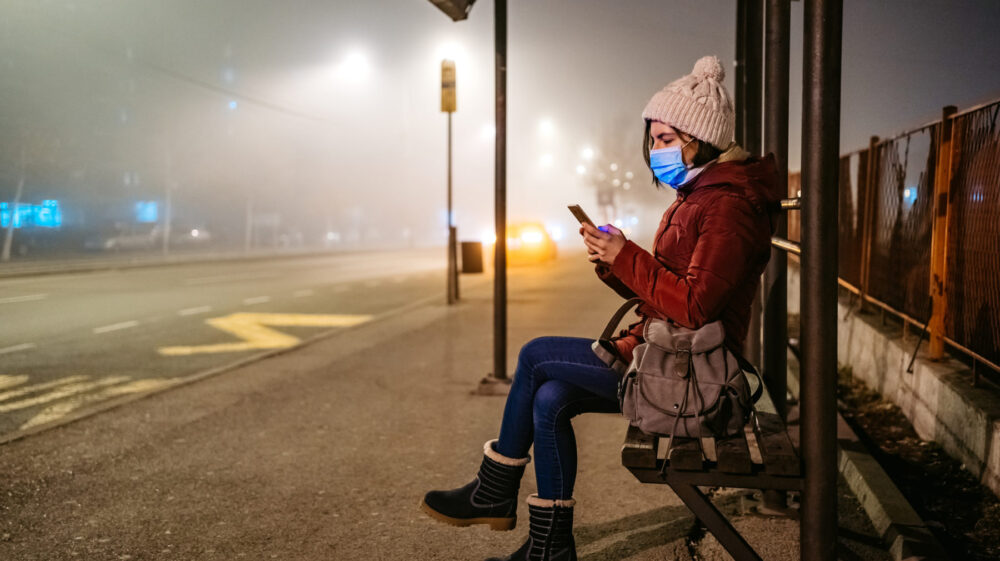 Woman with mask using phone on bus stop