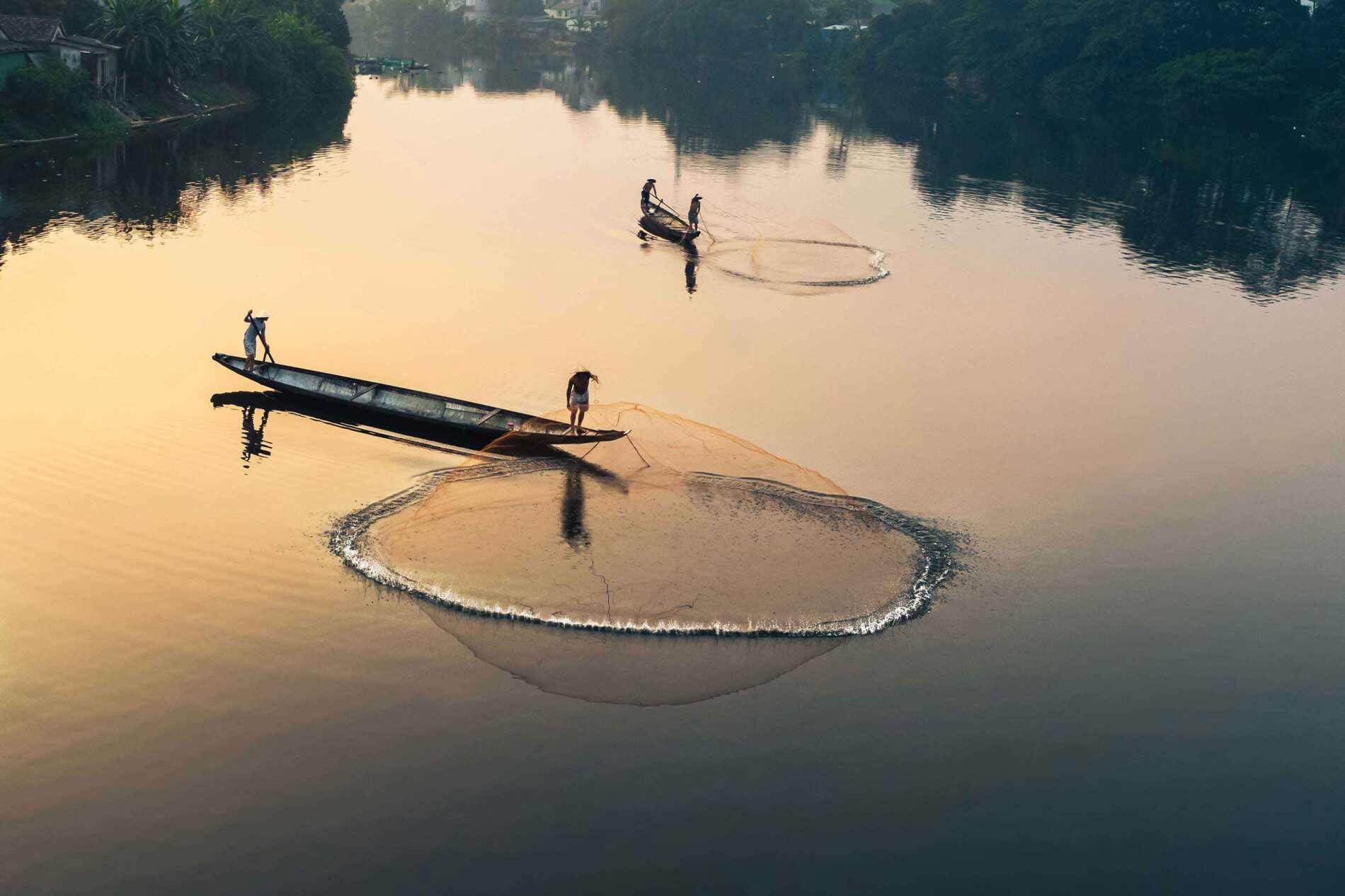 Two (2) boats on the Perfume River, Vietnam. Two (2) fishermen in each boat stand casting nets into the water.