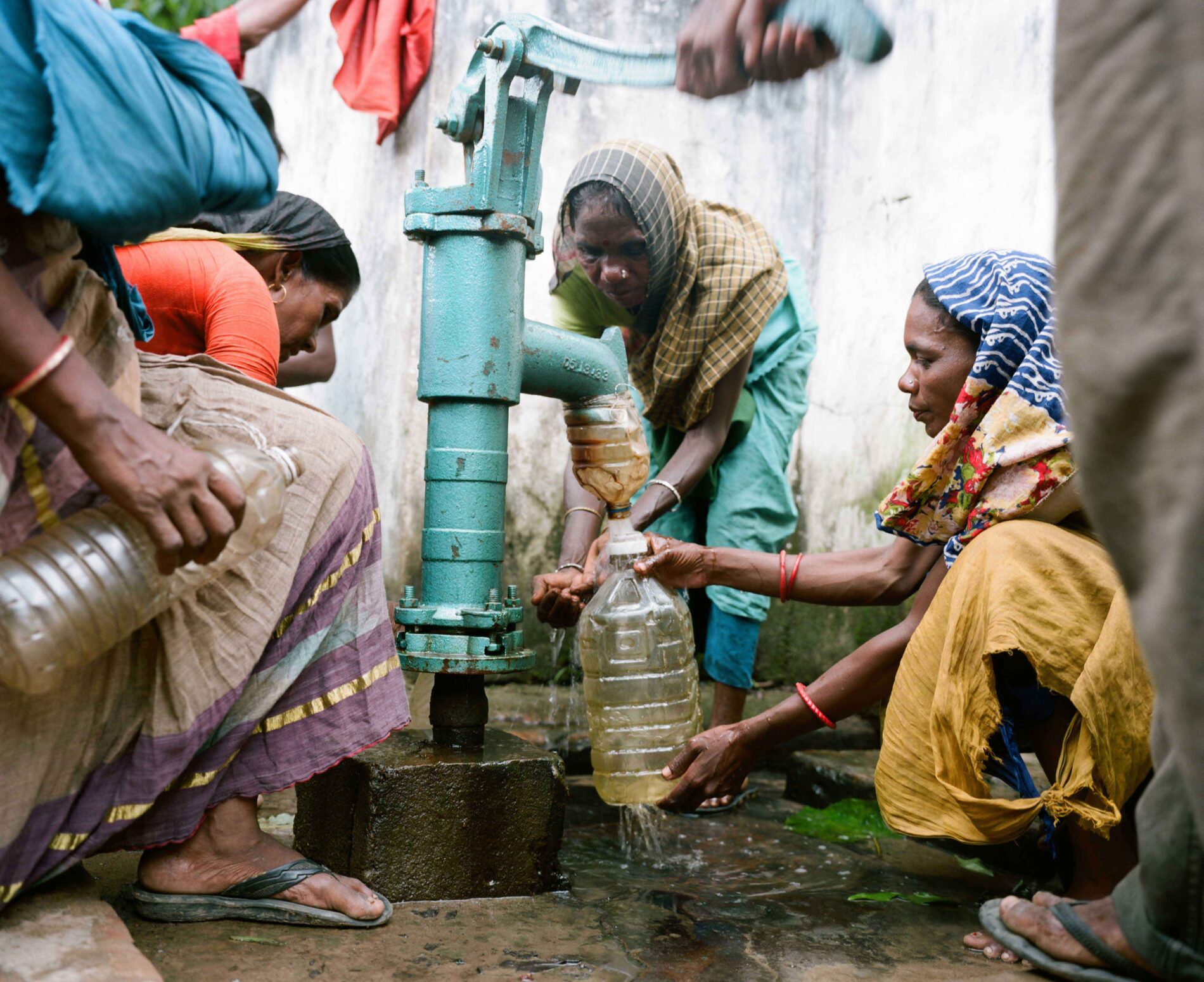 A group of women around a water pump collecting water in plastic bottles.