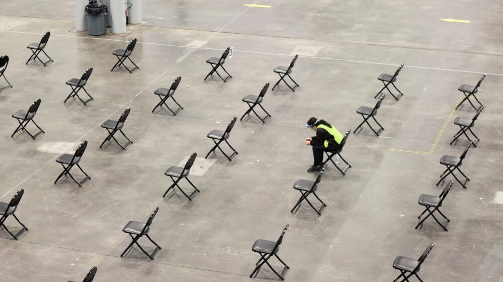 Worker sits on chair in empty vaccination centre