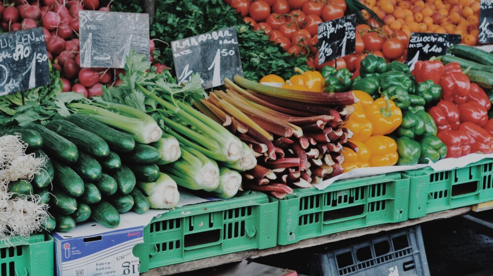 Fruit and vegetable stand at a farmer's market with cucumbers, celery, rhubarb, yellow, green and red bell peppers, radishes, parsley, tomatoes and apricots