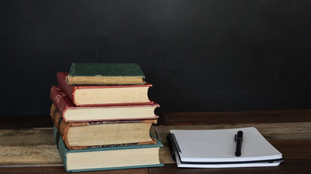 Stack of books and notebook with pen on desk