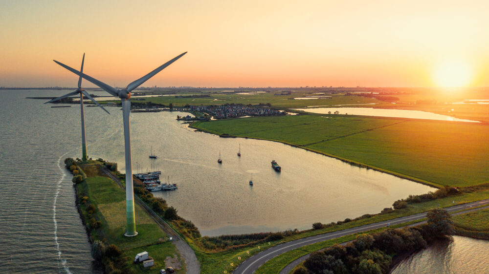 Aerial photo of wind turbines and setting sun on road connecting Dutch mainland to former island of Marken with Markemeer surrounding wind turbines