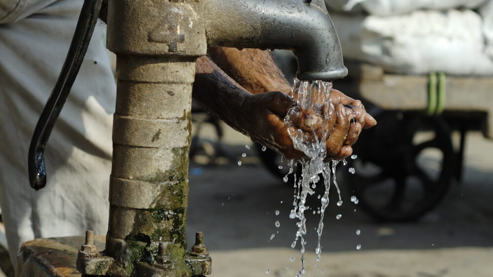 Man washing his hands at an old-fashioned water pump, street scene in Old Delhi