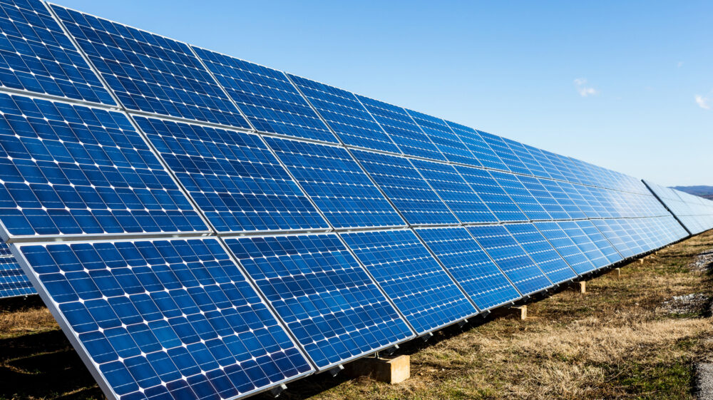 Row of blue photovoltaic solar panels and blue sky with clouds